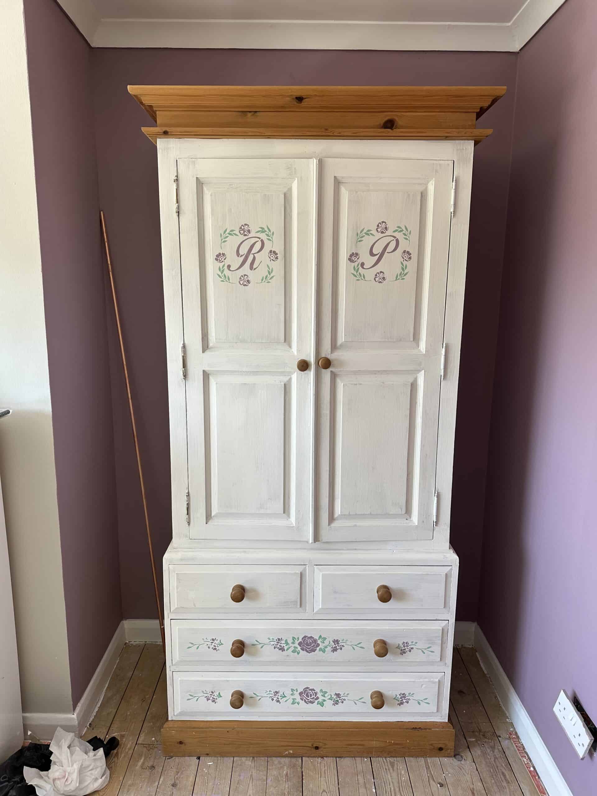 White wooden wardrobe with floral monograms and drawers, custom painted by Kingfisher Creative House.